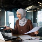 Young muslim businesswoman in hijab working in office with documents and talking on video call from