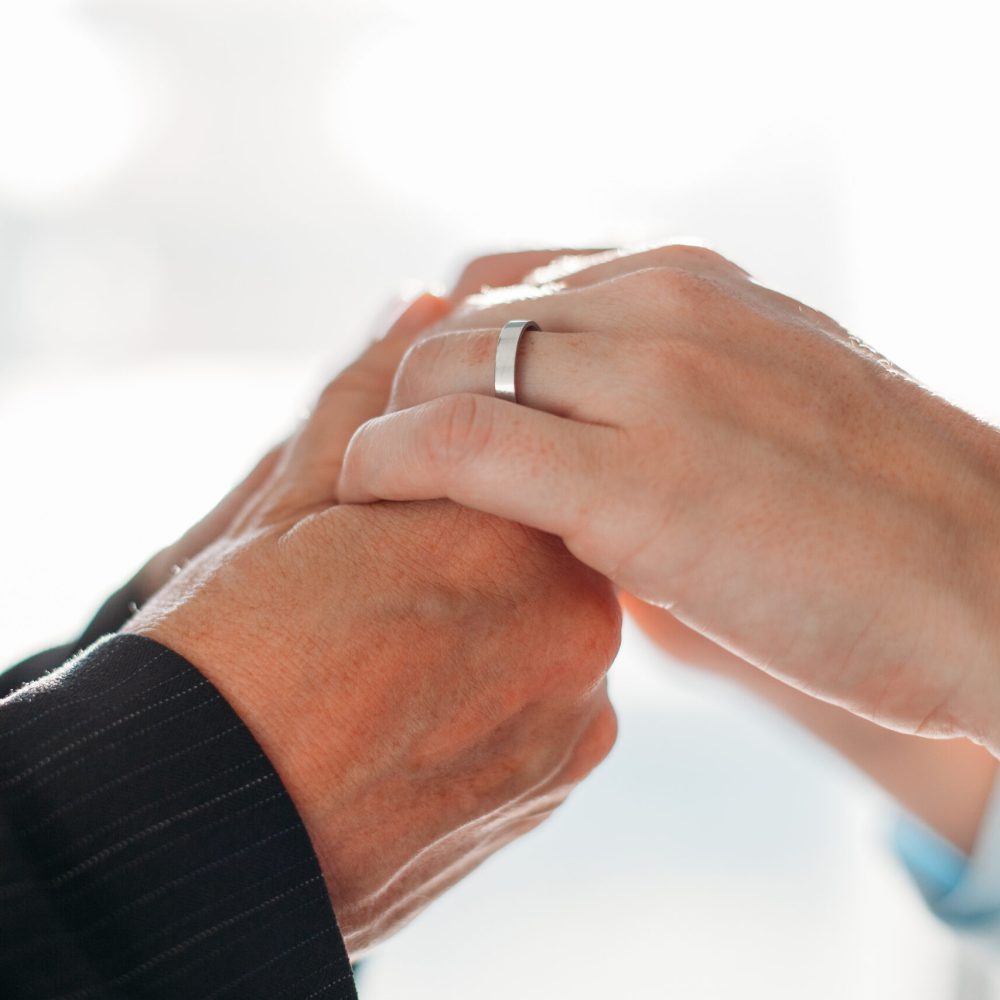 Close-up of unrecognizable man holding wifes hands with wedding ring in sunlight. Man taking care of woman or supporting her. Love confession or relationship concept